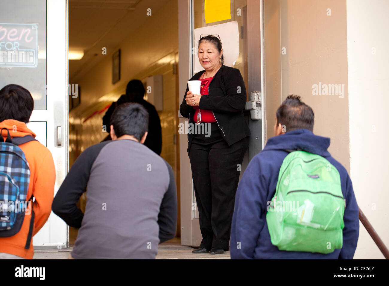 Hispanic teacher welcomes students to school at the entrance door of Highland High School Stock Photo