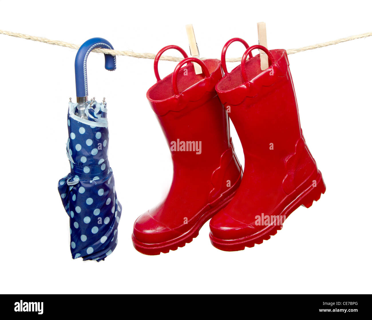 Red rain boots and a blue umbrella hang to dry on a clothes line. Isolated on a white background Stock Photo