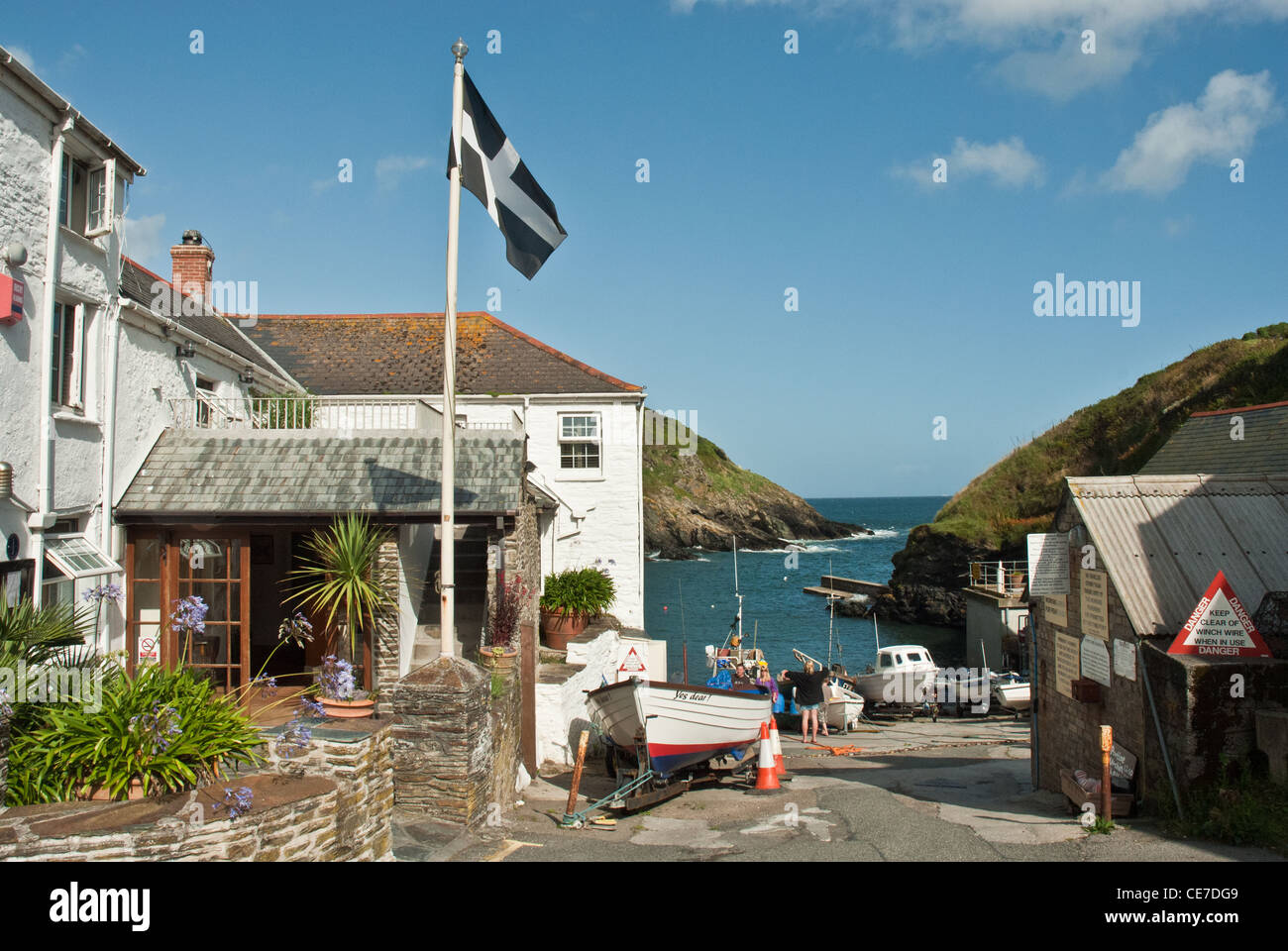 Portloe Cove and Harbour in summer with Cornish flag, small boats, traditional fishing cottages, blue sea and sky. Stock Photo