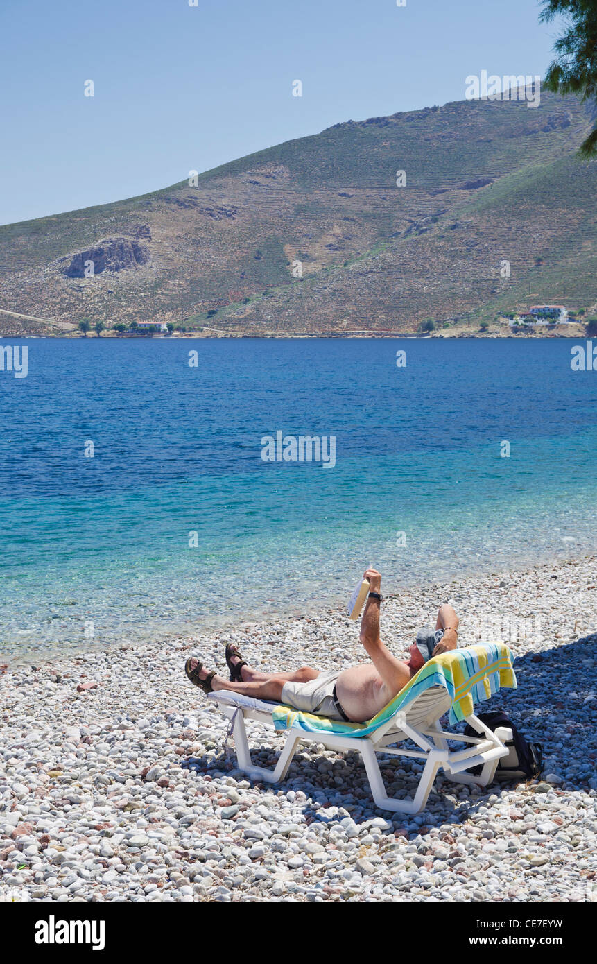 Man reading a book on a beach sun lounger on Tilos Island, Greece Stock Photo
