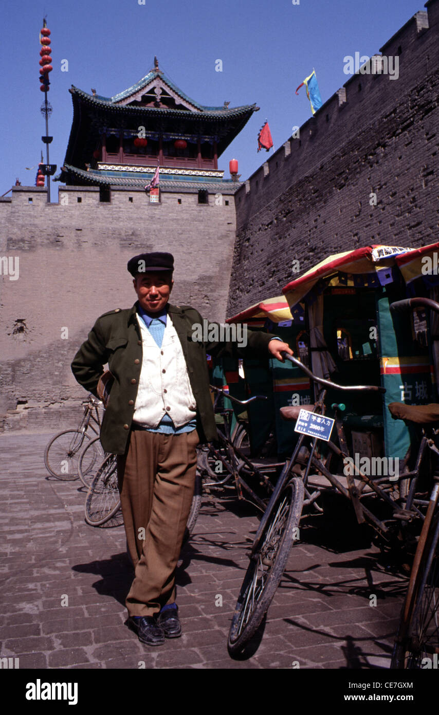 A rickshaw pedicab driver beneath the ancient Ming walls in the city of Ping Yao officially Pingyao Ancient City in central Shanxi, China Stock Photo