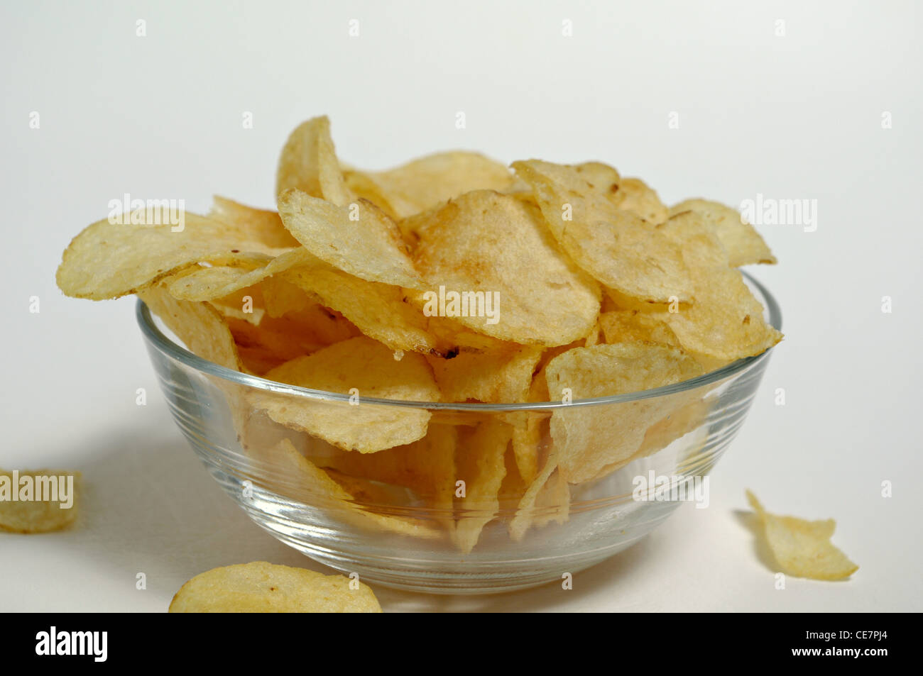 Potato chips sit in a glass bowl on a plain white background. Stock Photo