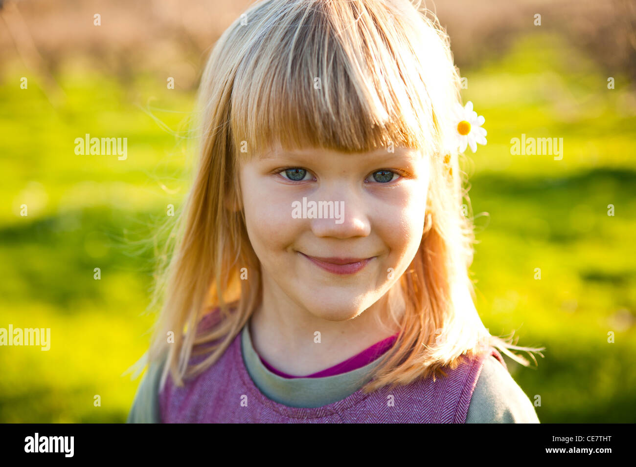 Cute little girl outdoors on a green field with flower in her hair ...