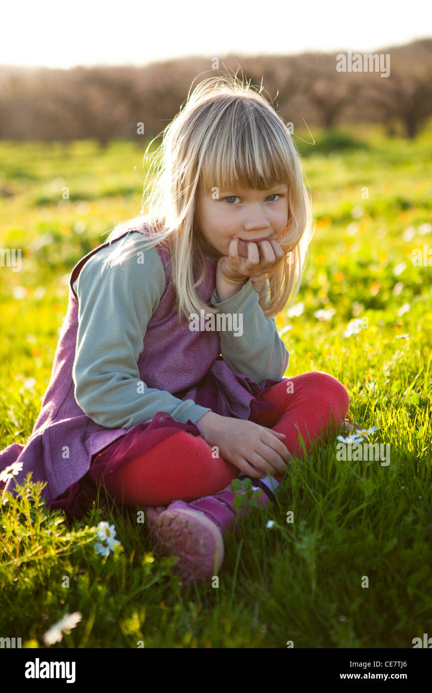 Cute little girl outdoors sitting on a green field with flowers Stock ...