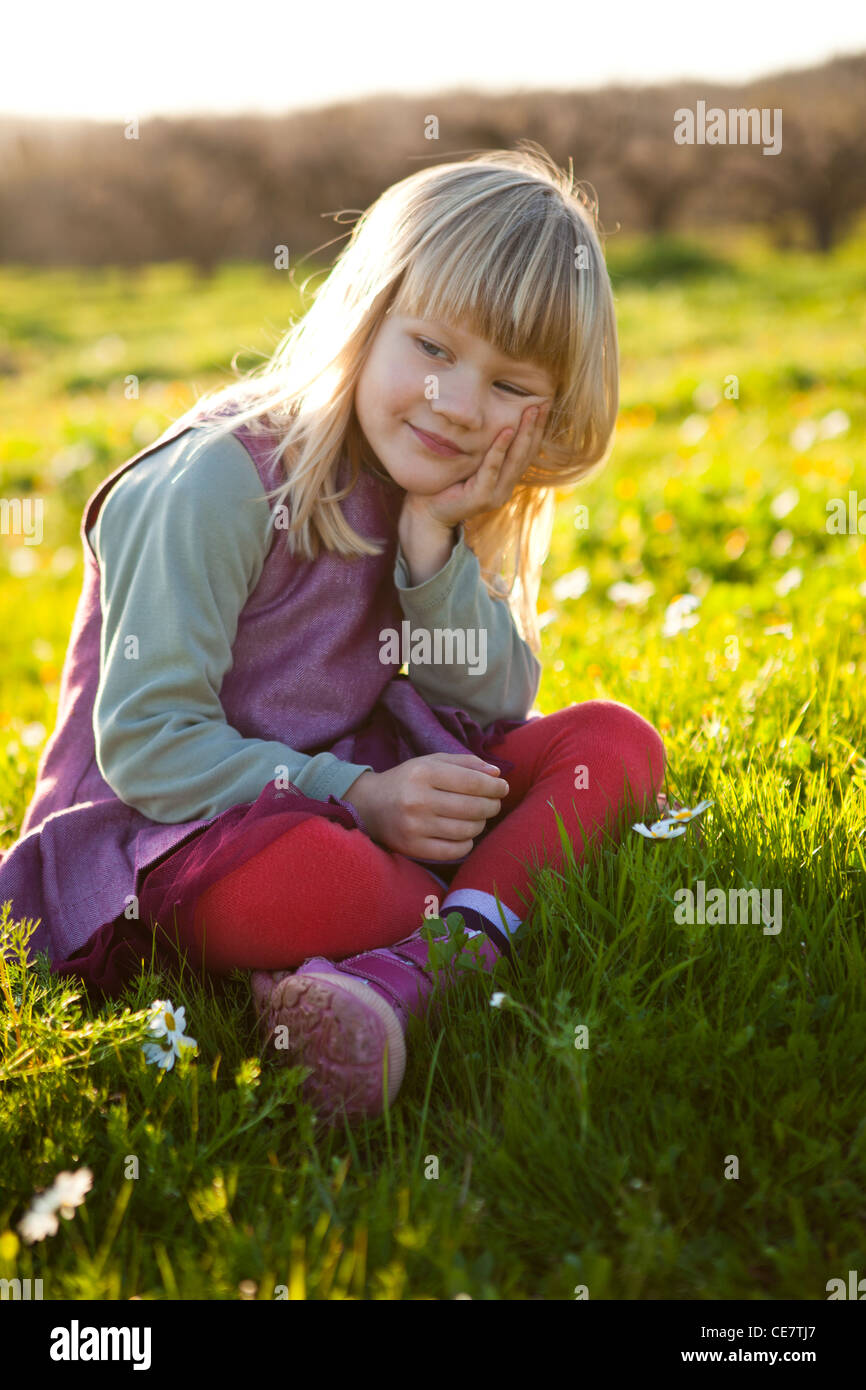 Cute little girl outdoors sitting on a green field with flowers Stock ...