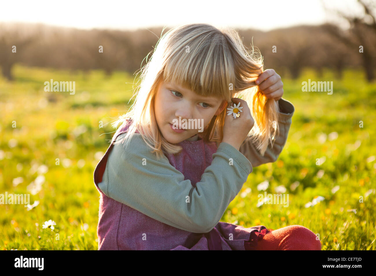 Cute little girl outdoors on a green field with flower in her hair ...