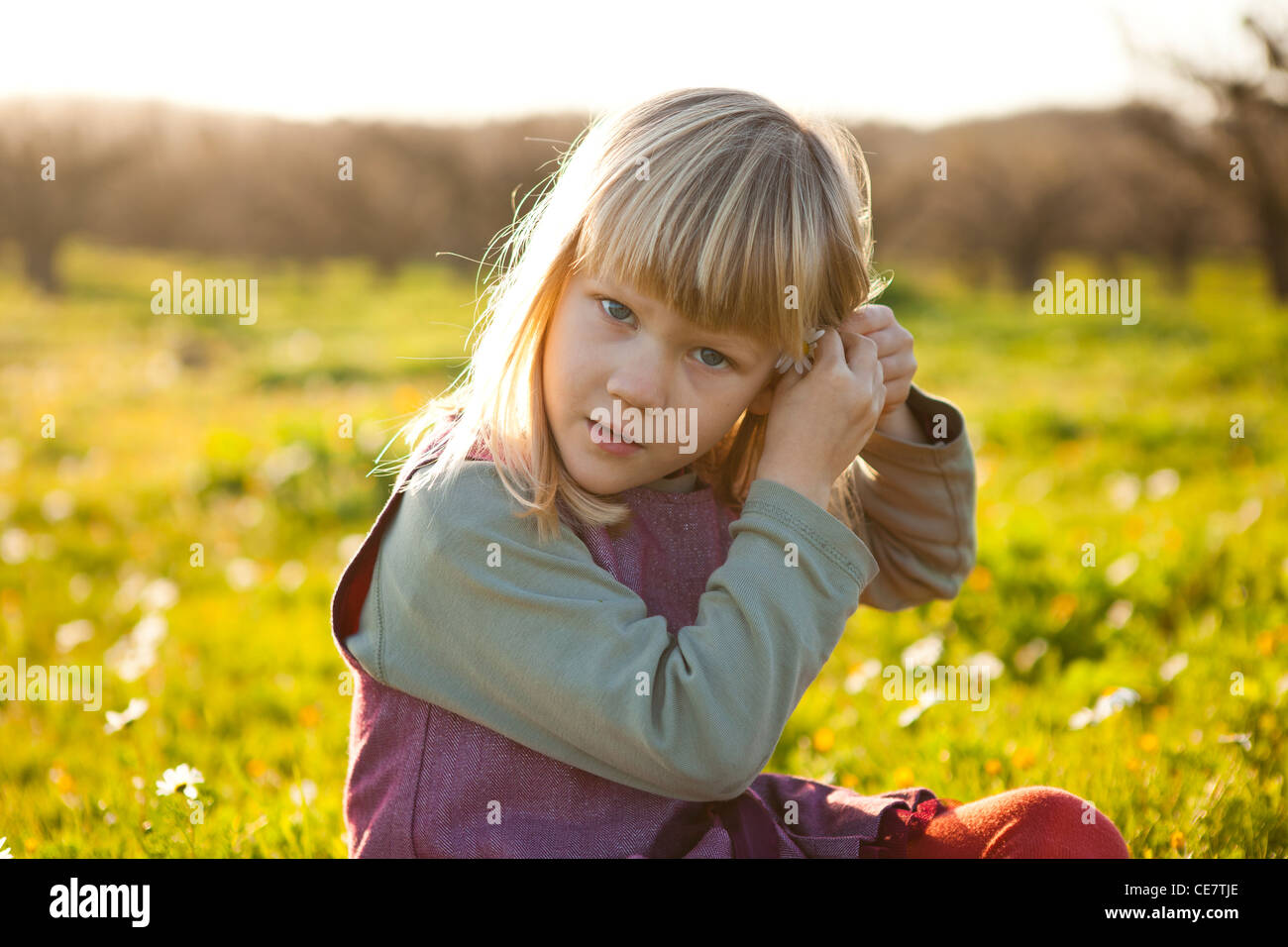 Cute little girl outdoors on a green field with flower in her hair ...