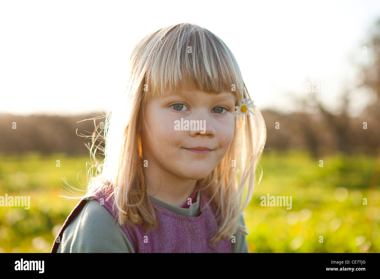 Cute little girl outdoors on a green field with flower in her hair ...