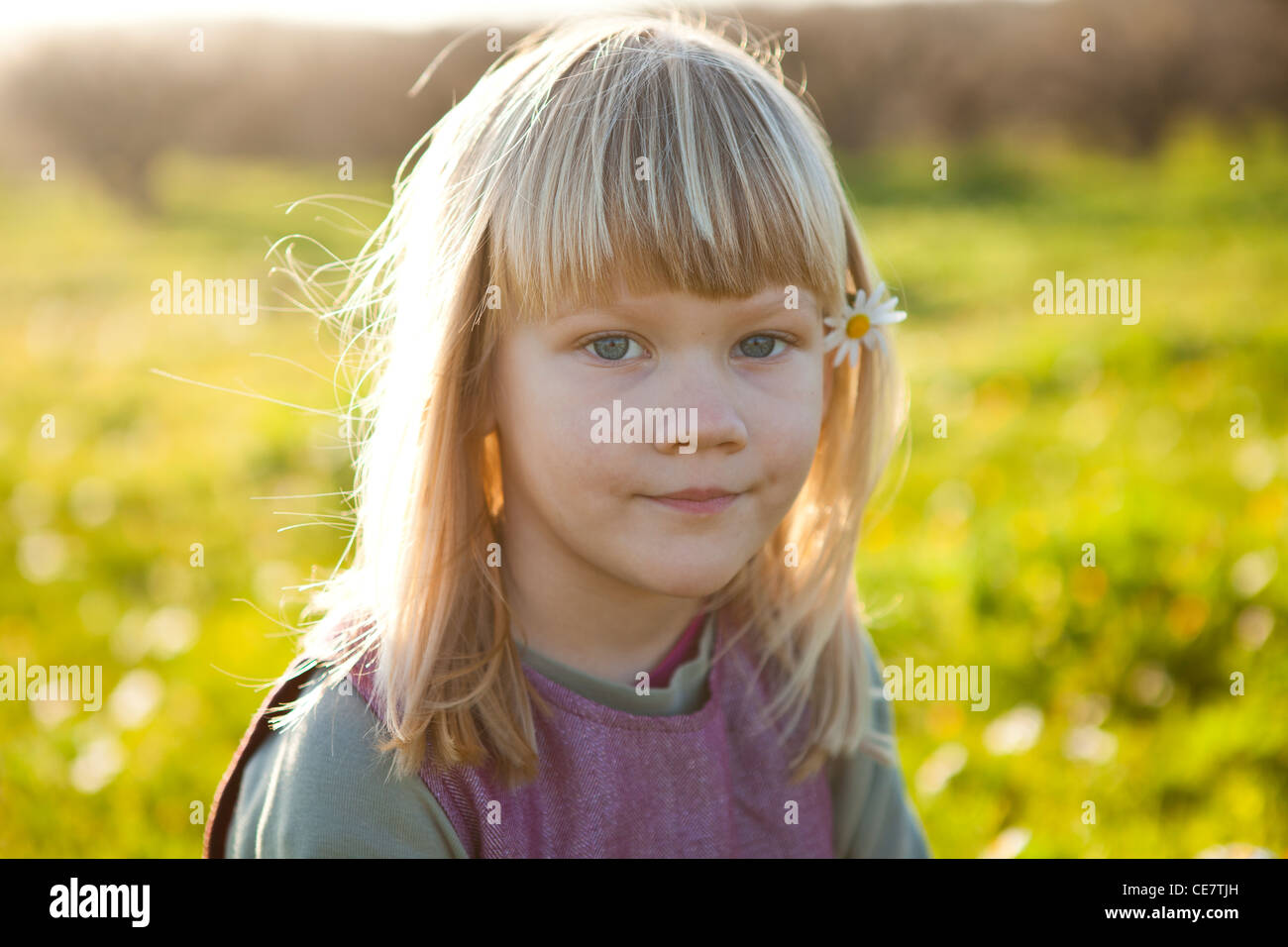 Cute little girl outdoors on a green field with flower in her hair ...