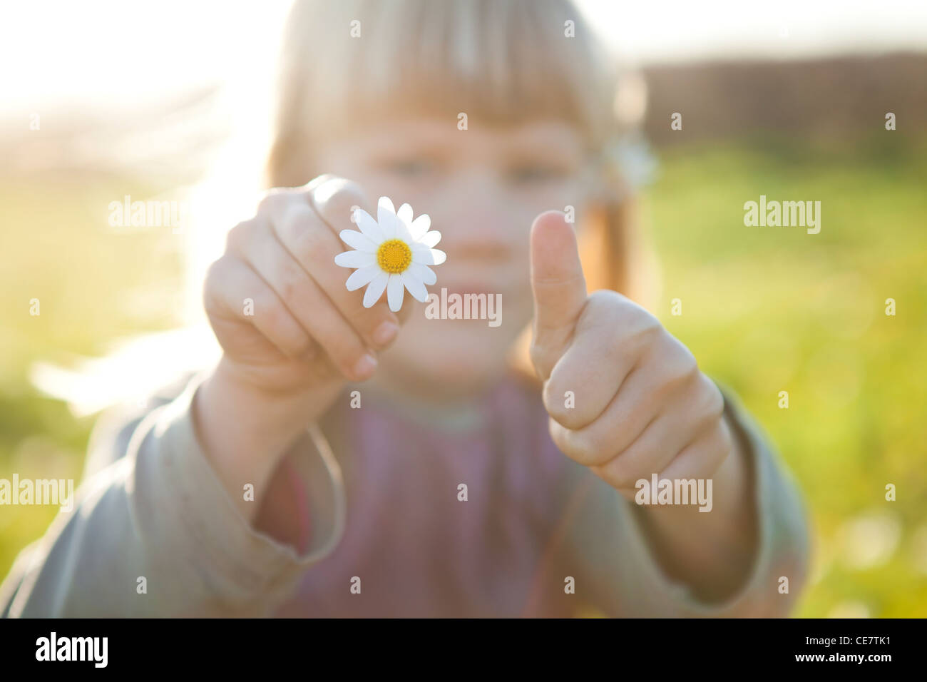 Cute little girl outdoors on a green field with a flower and thumbs up ...