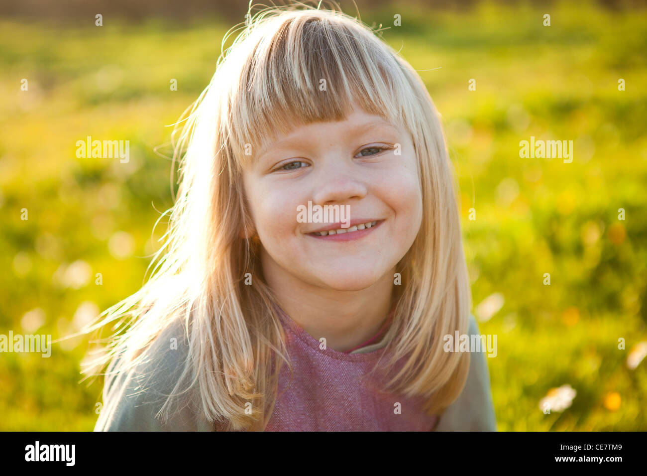 Cute little girl outdoors on a green field with flowers Stock Photo - Alamy