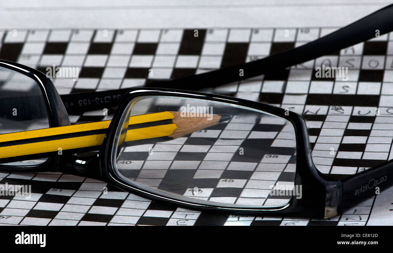 A pair of reading glasses lying upturned on top of a large incomplete crossword with a pencil Stock Photo