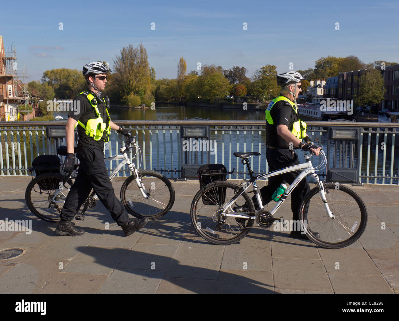 Two policemen in fluorescent jackets wheeling their bicycles across Windsor Bridge over the River Thames Stock Photo