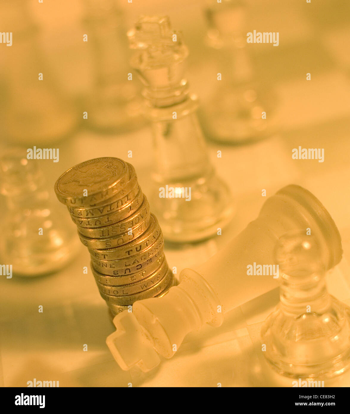 A pile of pound / sterling coins on a chess board surrounded by chess pieces. The image depicts financial,business strategies. Stock Photo