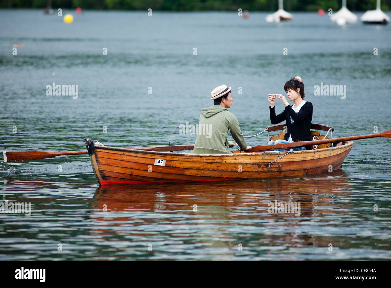 An Asian couple in a wooden rowing boat for hire on Lake Windermere. She is taking a photograph