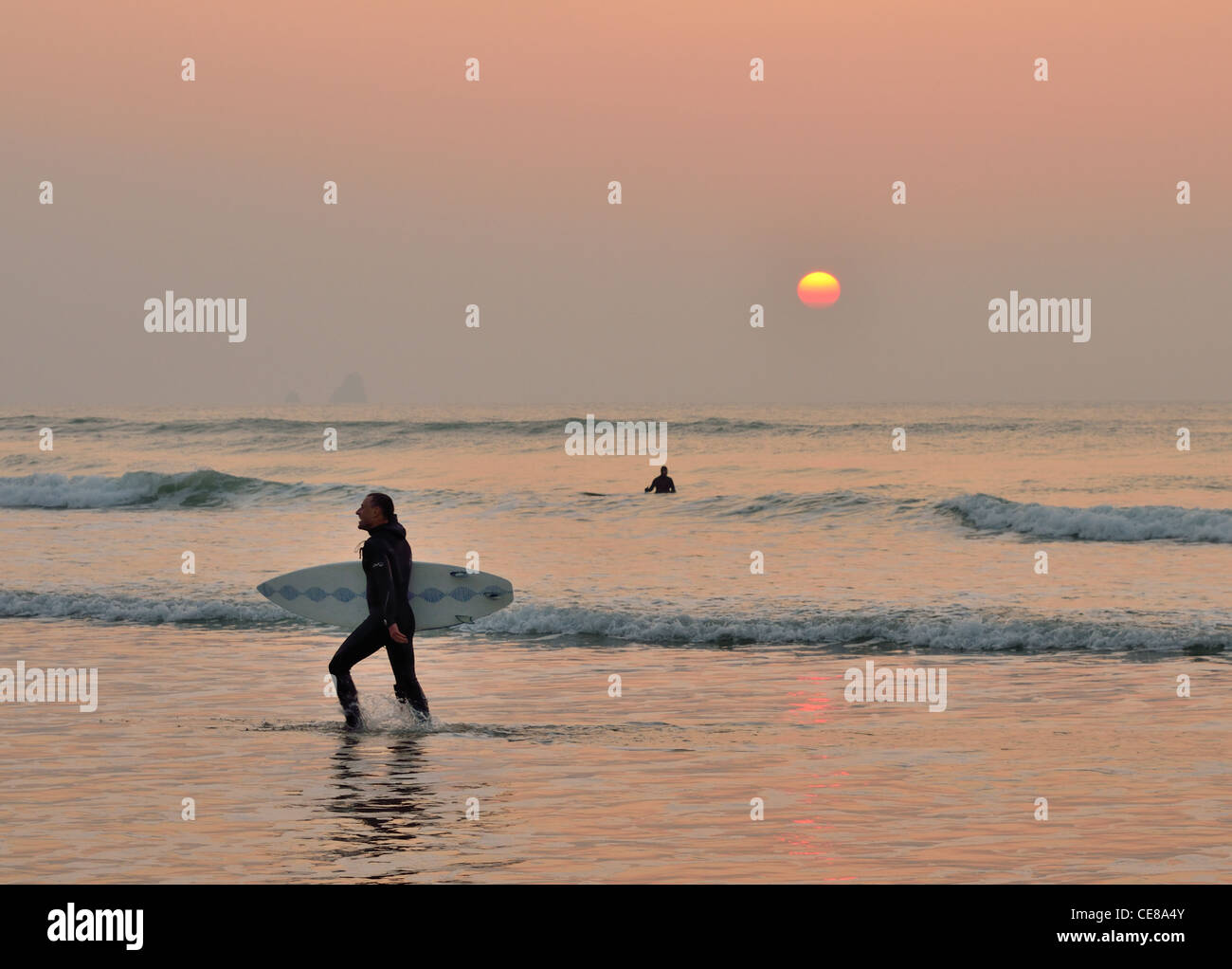 Happy Surfer leaving the sea as the sun sets casting a hazy orange glow Stock Photo