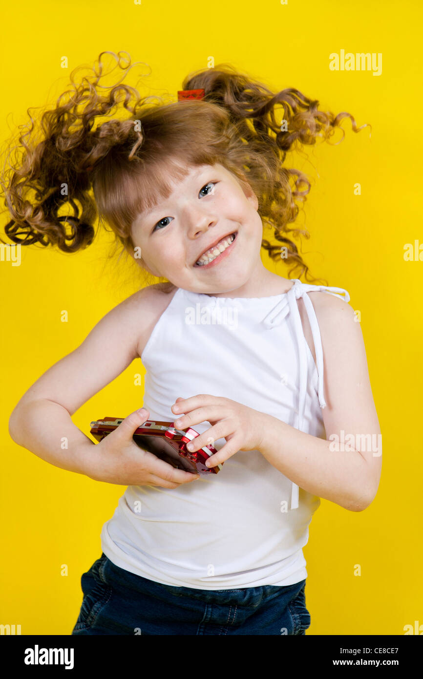 Little girl playing handheld portable game console. Yellow background Stock Photo