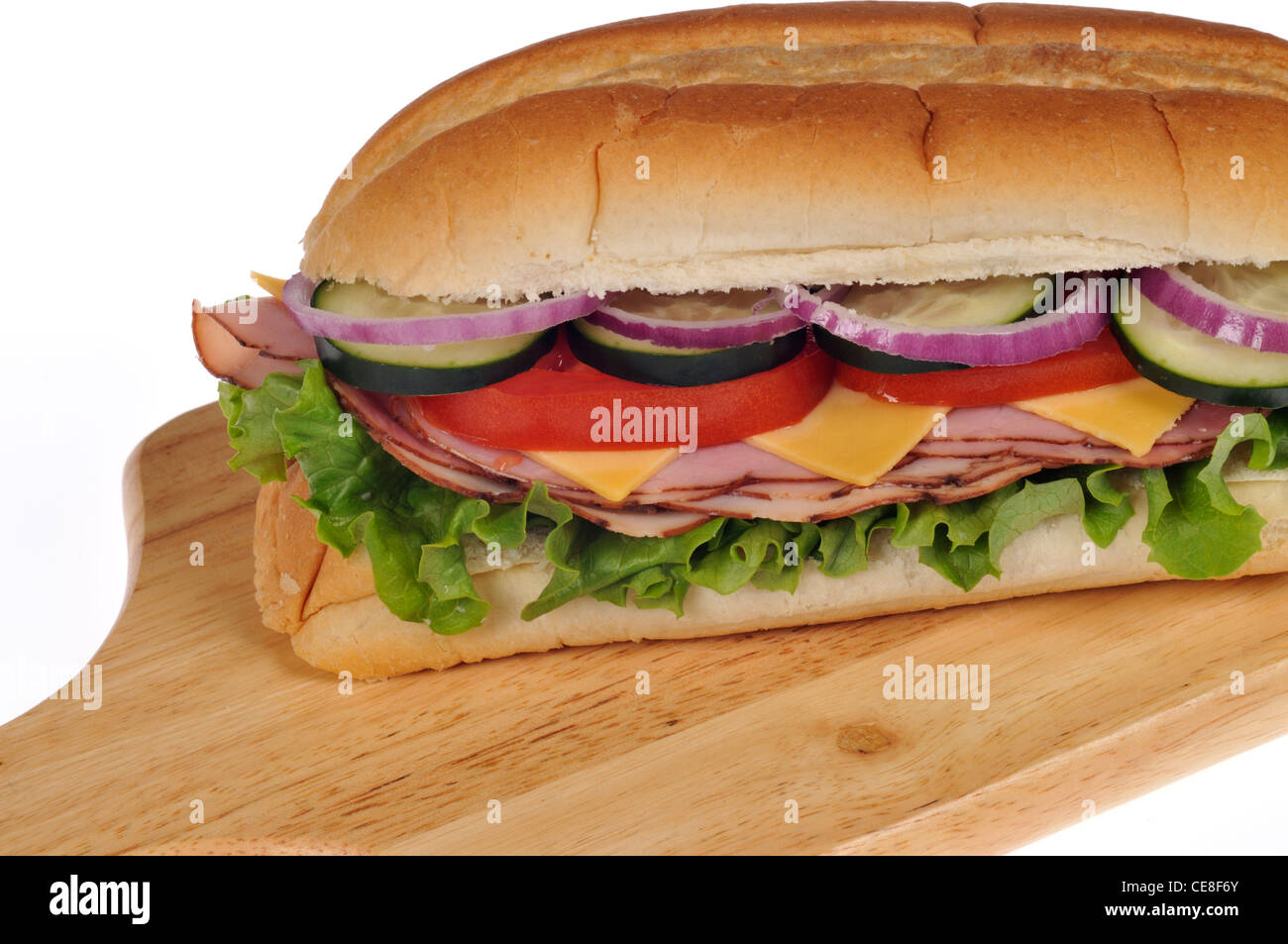 Closeup of ham and cheese sub sandwich with lettuce tomatoes onions and cucumber on wood deli board on white background Stock Photo