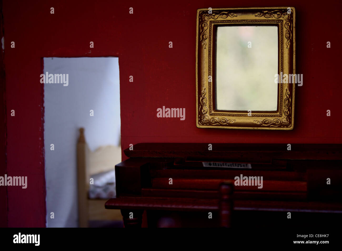 Dolls house mirror and piano, with bedroom in the background doorway. Stock Photo