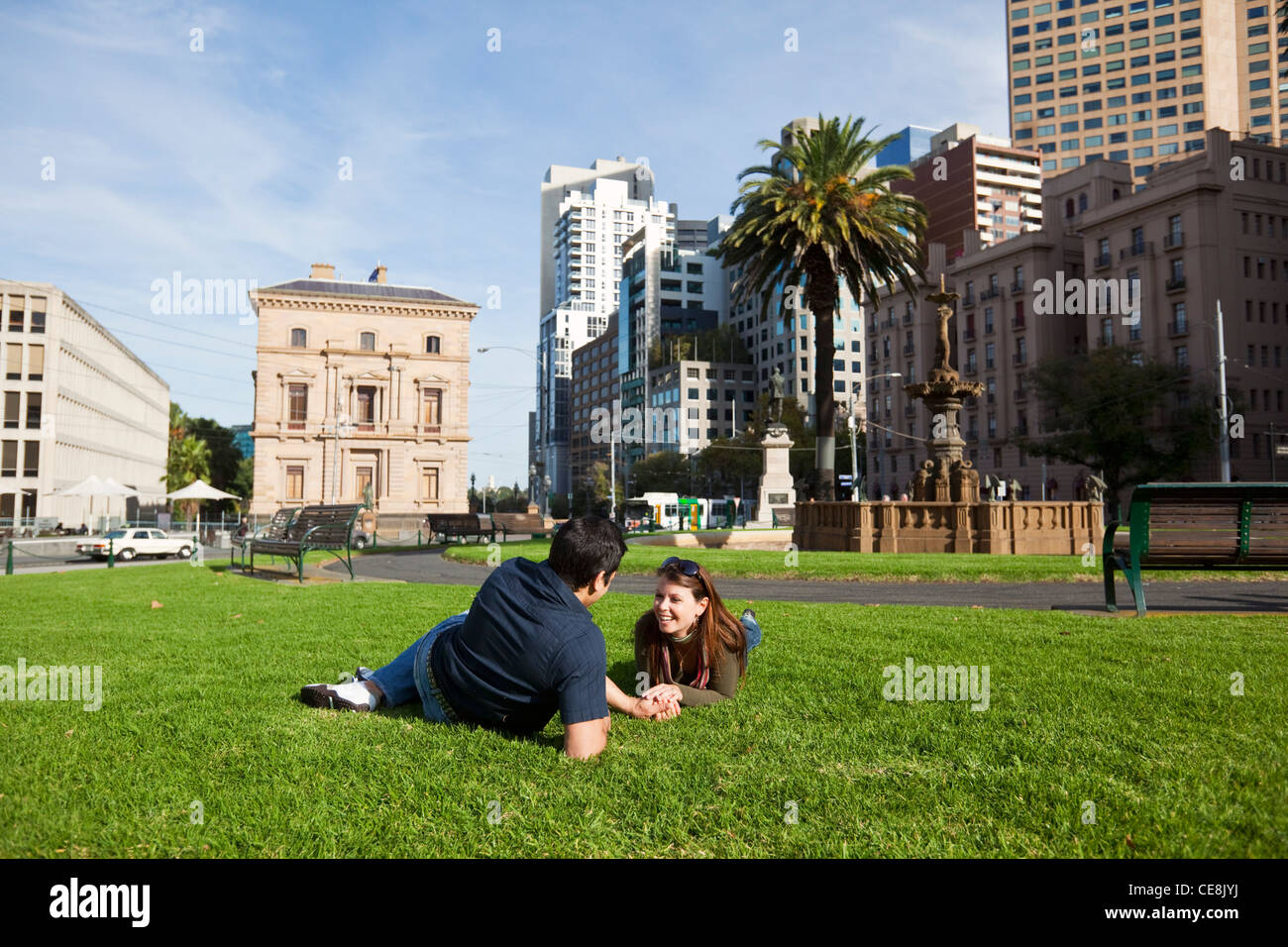 Young couple relaxing in park with city skyline in background. Gordon Reserve, Melbourne, Victoria, Australia Stock Photo