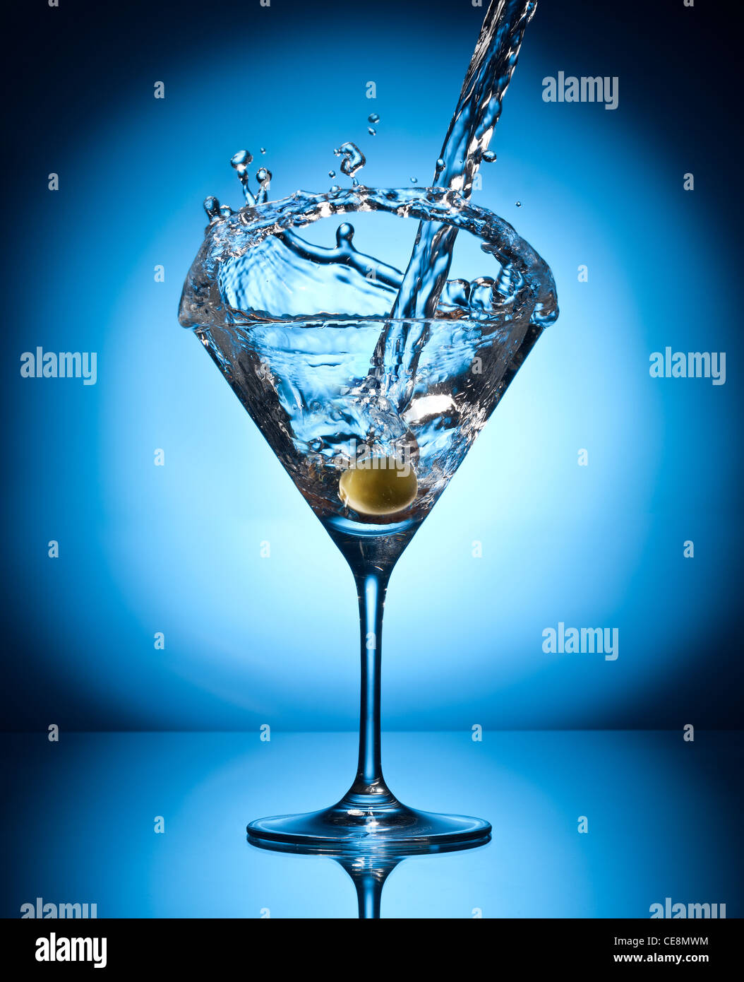 Splash martini from flying olives. Object on a blue background. Stock Photo