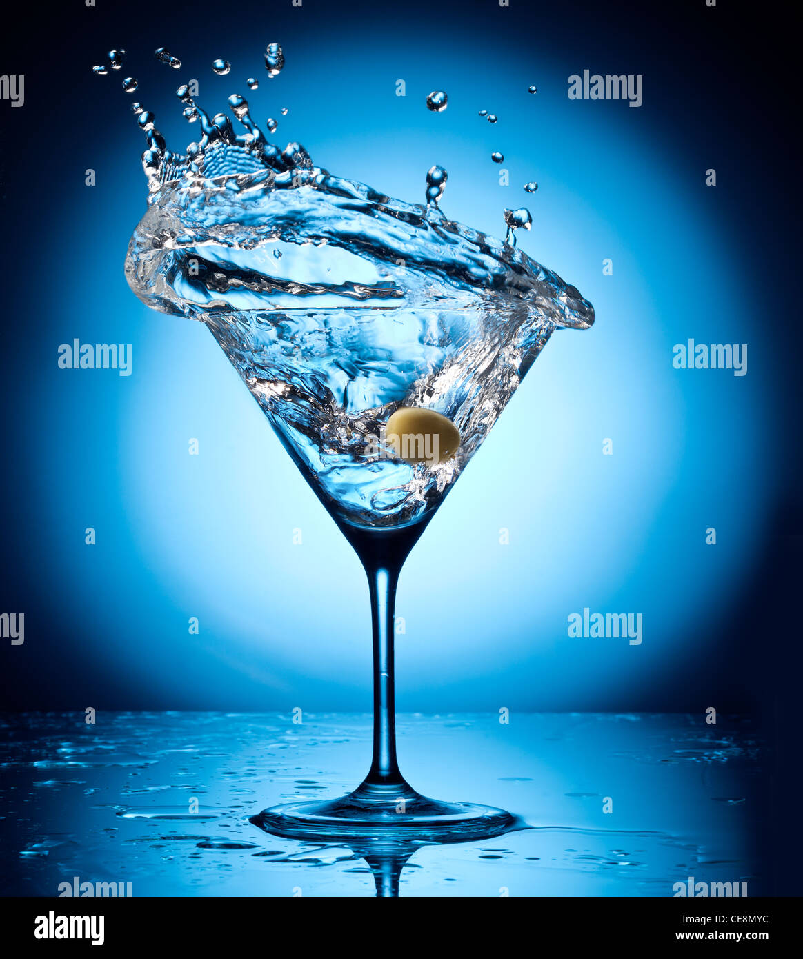 Splash martini from flying olives. Object on a blue background. Stock Photo