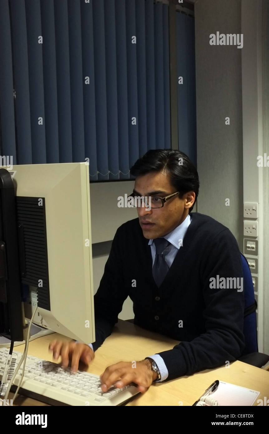A male office worker sat at computer in contemporary office setting. Stock Photo