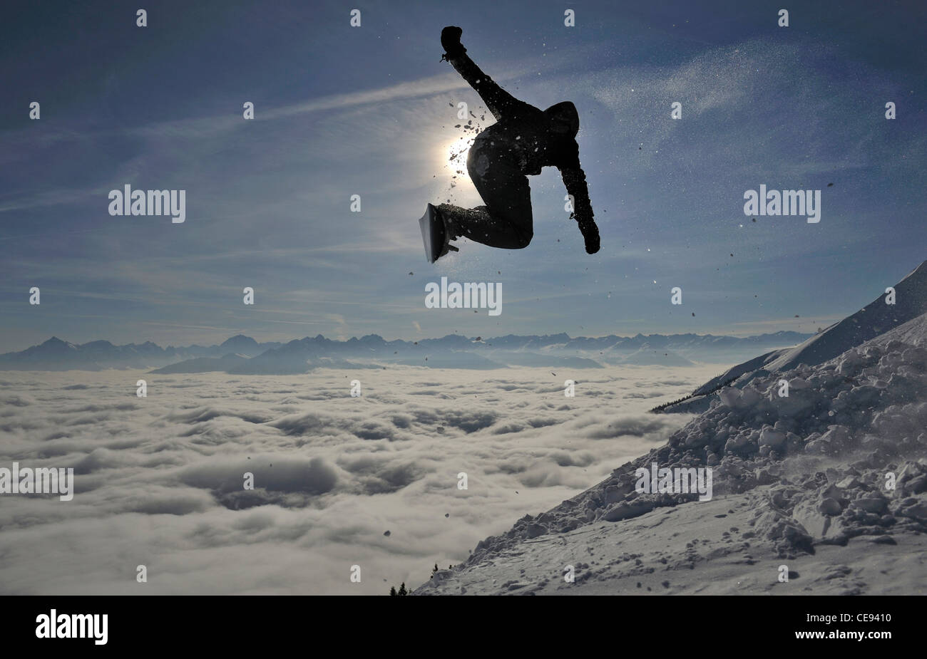 Snowboarder jumps off a mountain against the dropping sun late in the day on the Nordkette mountain above Innsbruck, Austria Stock Photo