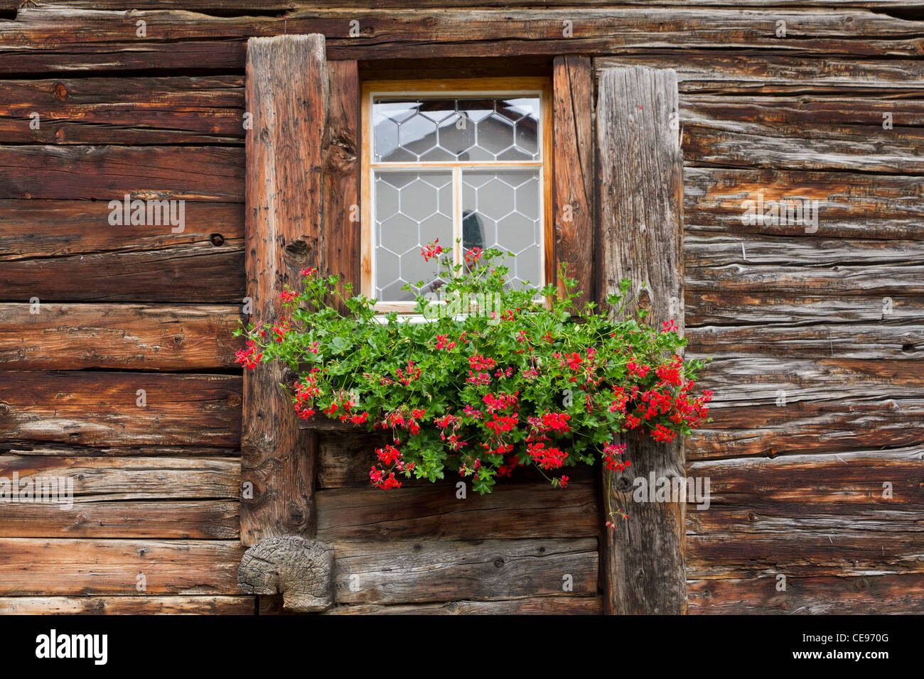window of a old wooden withered house decorated by red geranium, Switzerland Stock Photo