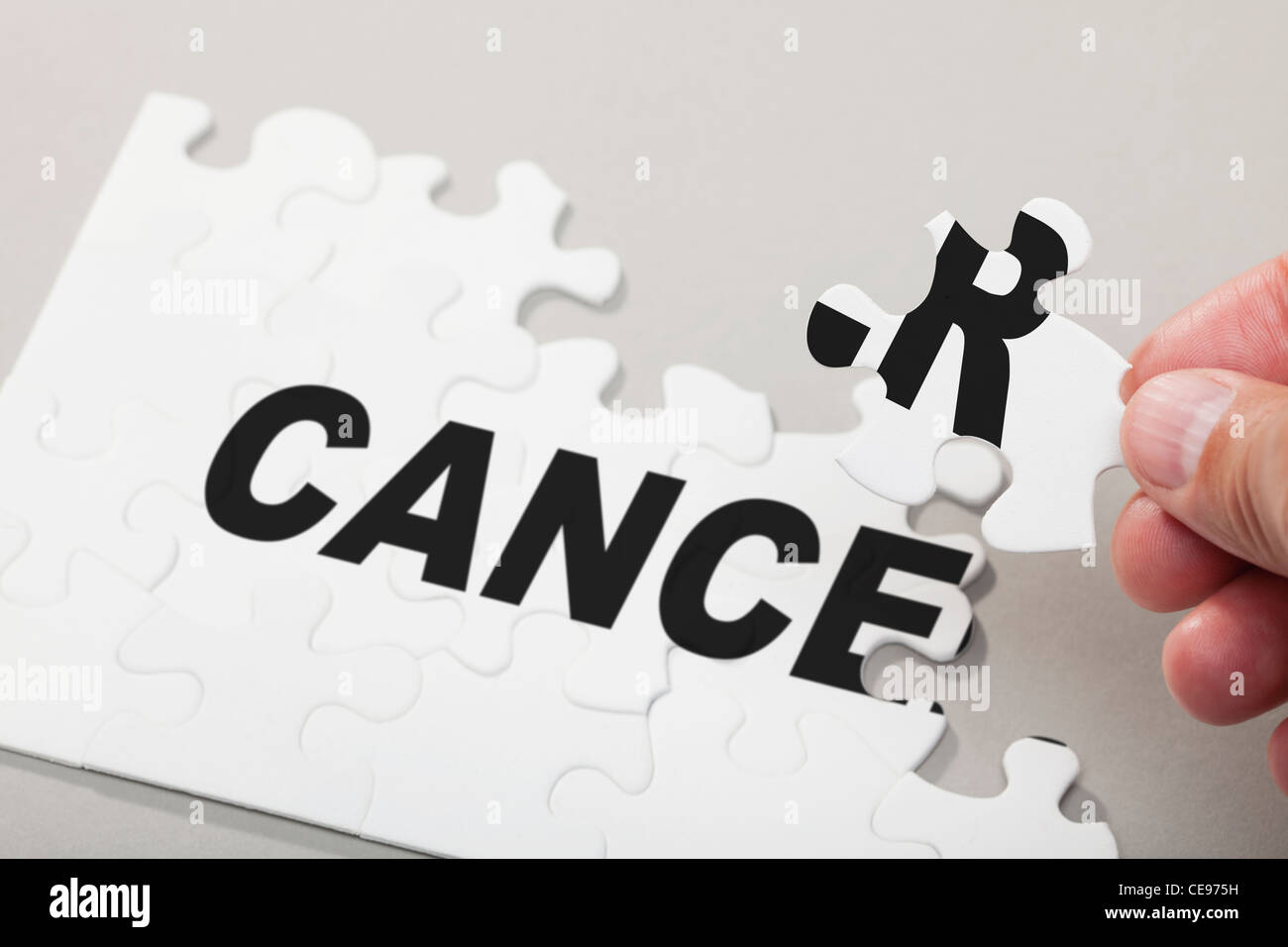Male hand arranging puzzle pieces spelling out CANCER Stock Photo
