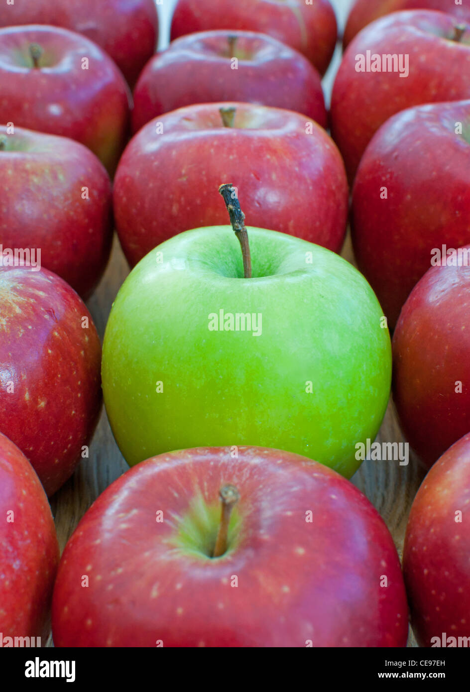 Single green apple standing out amongst many red apples Stock Photo