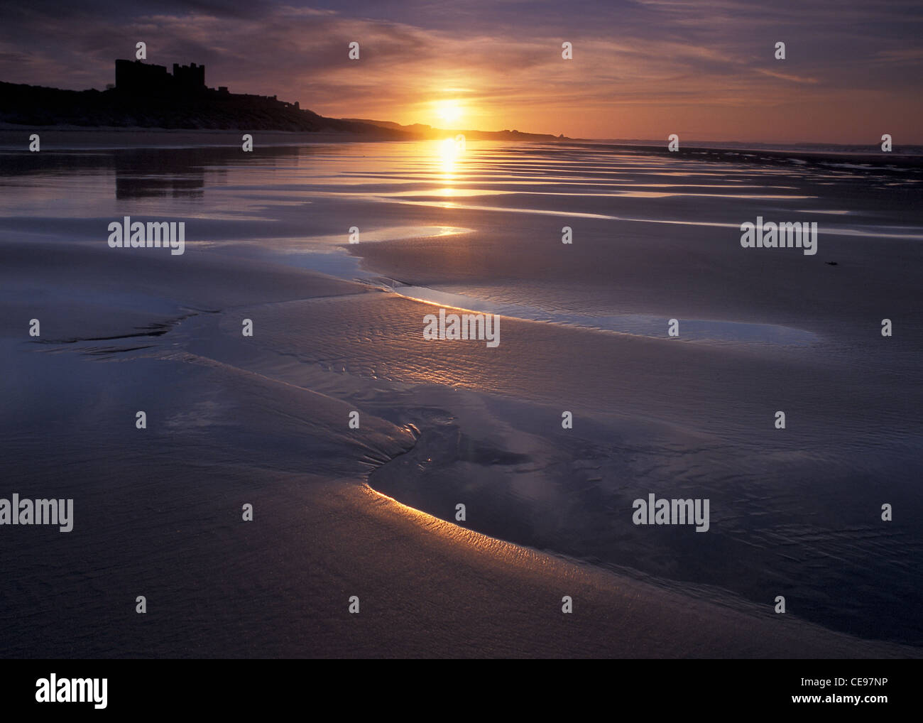 Bands of wet and dry sand left by the retreating tide catch the spring sunset at Bamburgh, Northumberland. Stock Photo