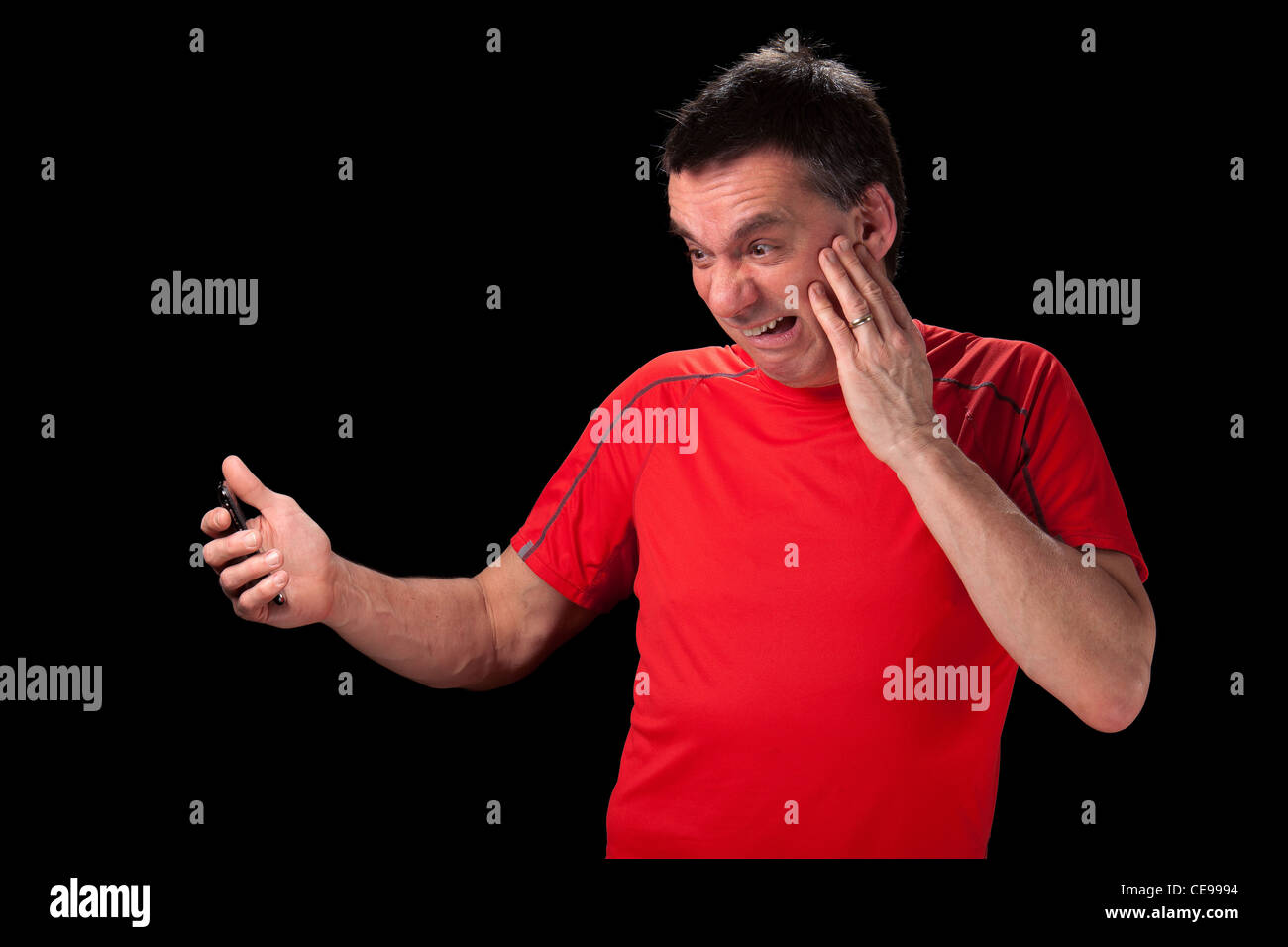 Middle Aged Man with horrified expression looking at phone in shock black background Stock Photo