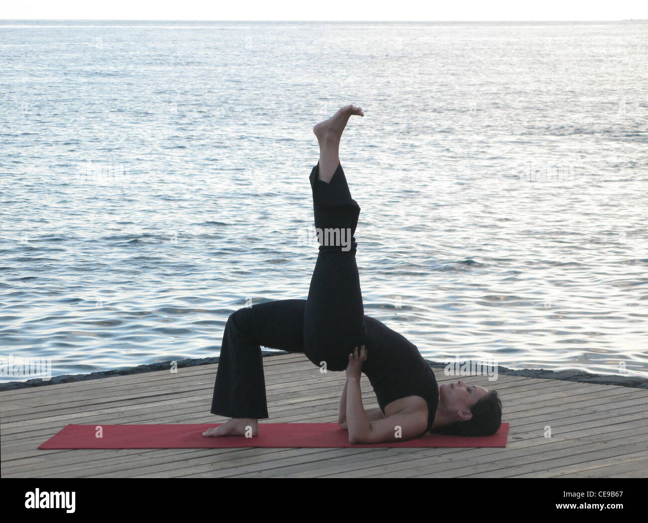 Yoga Pose Woman doing Setu Bandha Sarvangasana (Bridge Pose Variation) with the ocean behind. Stock Photo