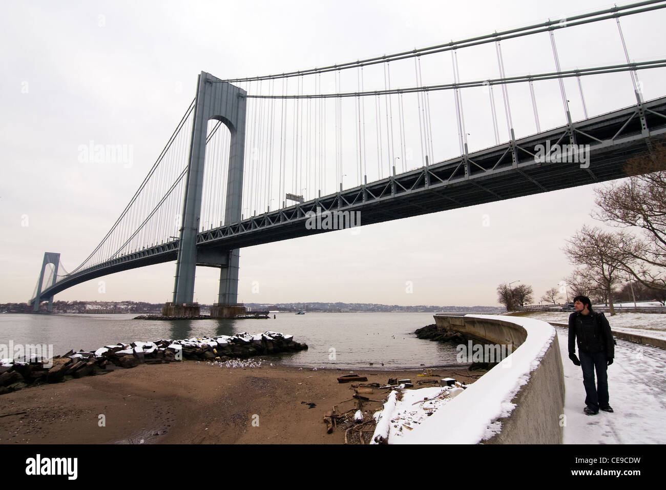 Man walking in snow under the Verrazano-Narrows Suspension Bridge in Bay Ridge Brooklyn, New York City Stock Photo