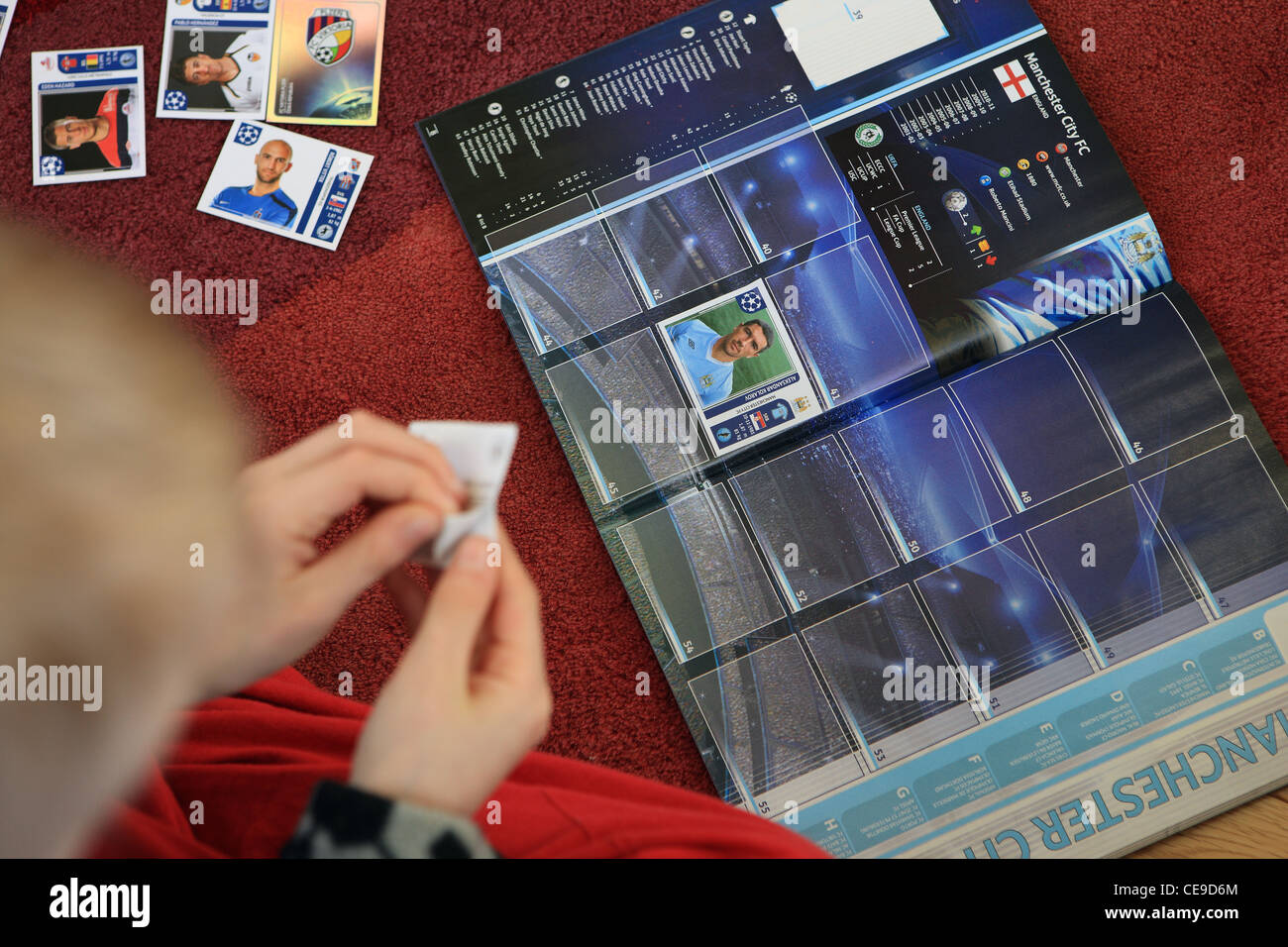 Young boy wearing pajamas and dressing gown sticking football stickers into a collection book Stock Photo