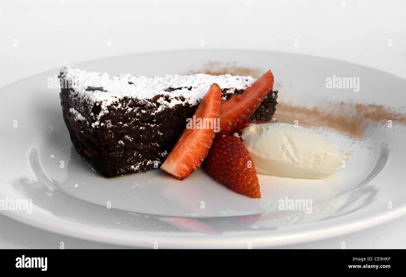 A slice of Chocolate Torte, accompanied by Creme Fraiche, Strawberry Wedges, and a dusting of Icing Sugar Stock Photo