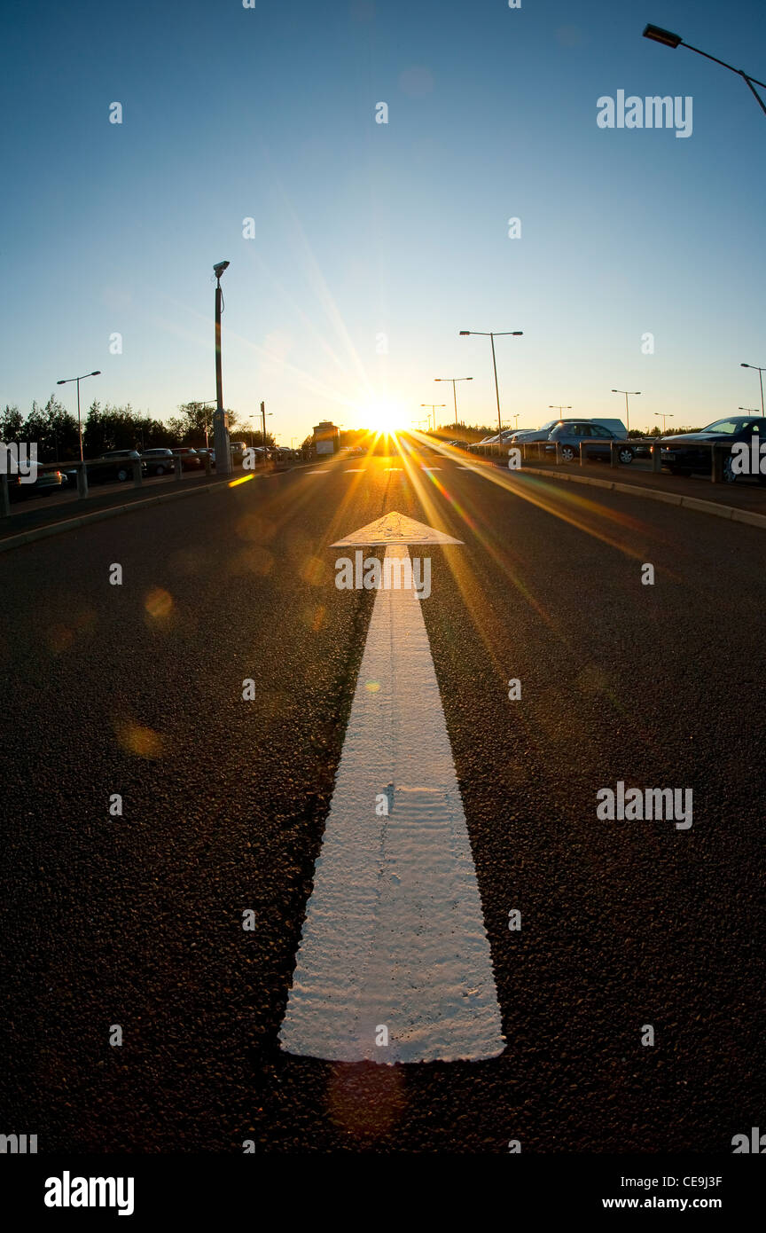 White arrow painted on the road in a car park in England at dusk. Stock Photo