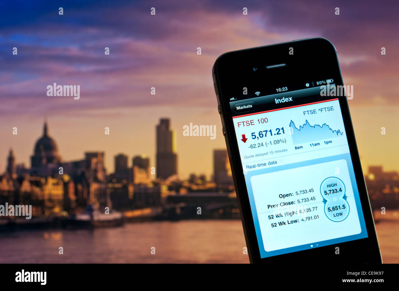 iPhone 4s screen displaying live trading day on FTSE 100 London Stock Markets with City of London and River Thames in background Stock Photo
