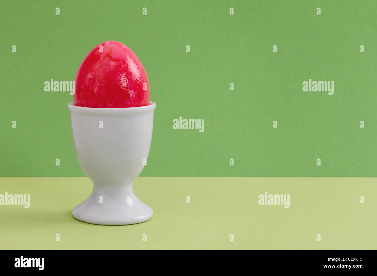 Red Easter egg in a white egg cup against a green background - studio shot with copy space Stock Photo
