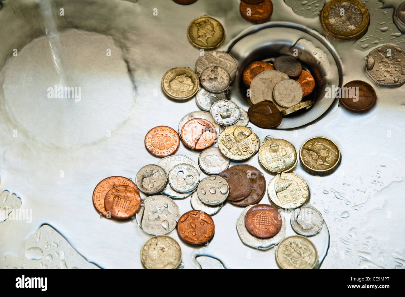 Down the plughole.  UK money down the drain. Coins and water down the drain. Stock Photo