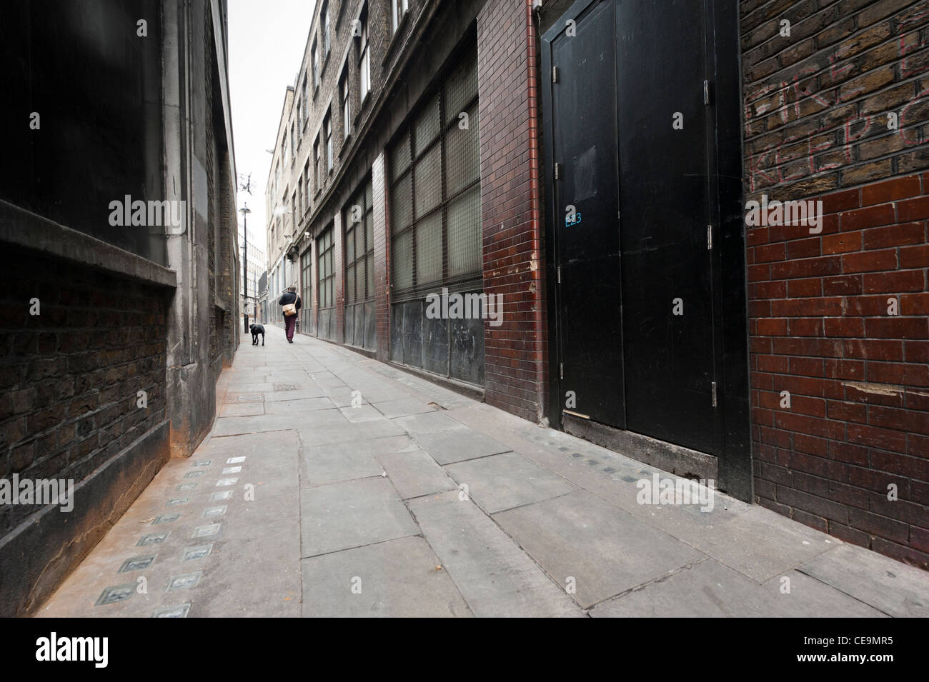 Alleyway or narrow street in central London with man walking dog in distance. Wide angle view Stock Photo