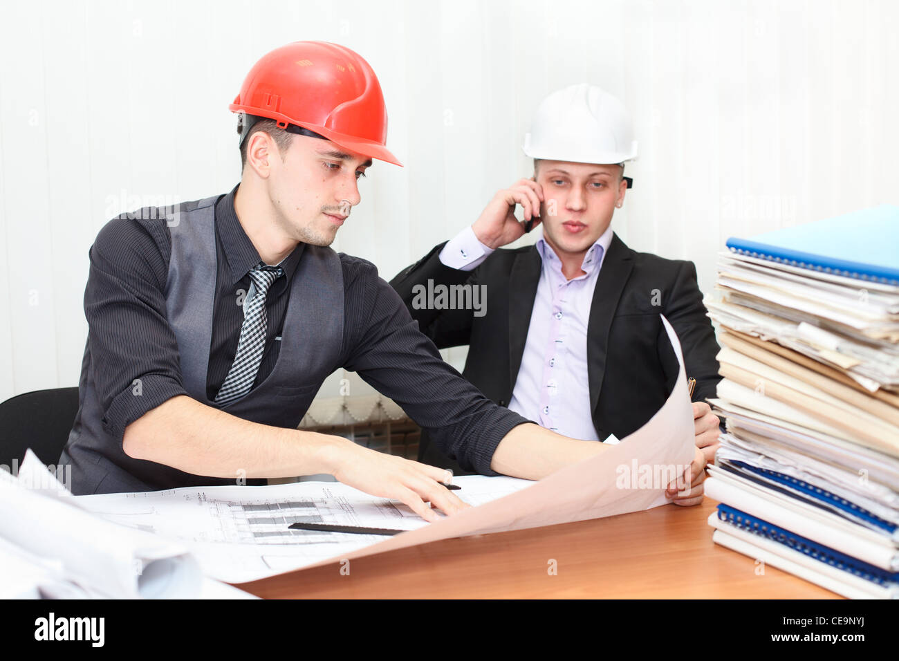 Architect and construction engineer discussing plan in office room. Caucasian people in helmets Stock Photo