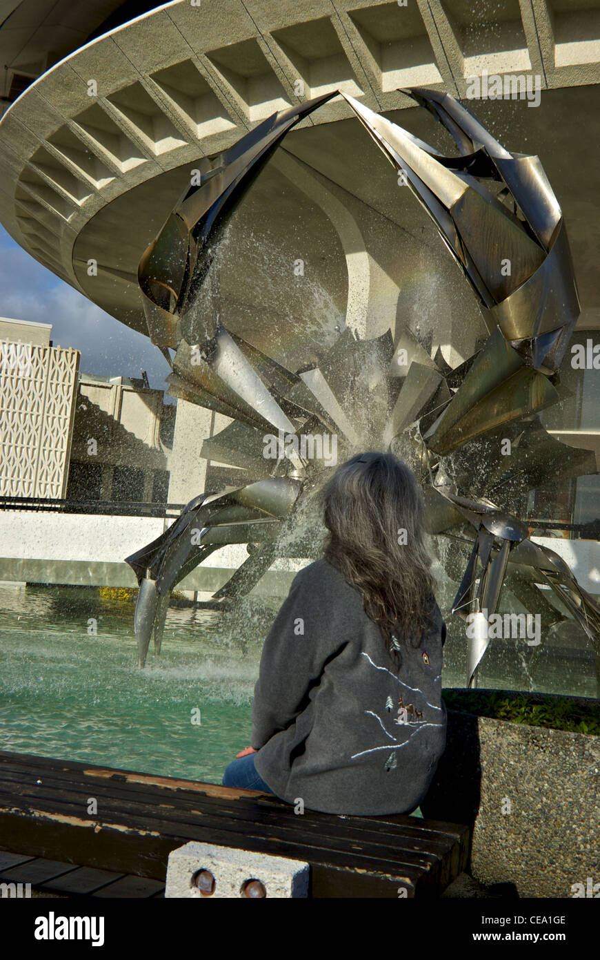 Woman sitting bench stainless steel crab sculpture fountain pool Vancouver Planetarium Stock Photo