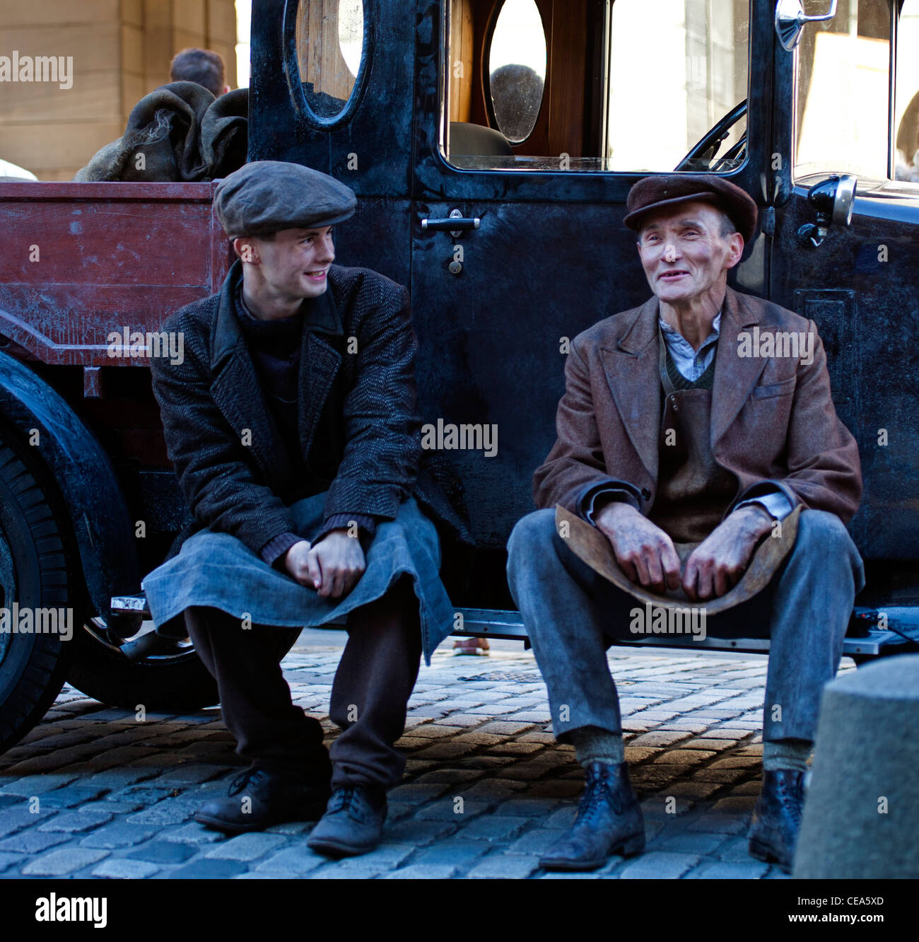 Man and boy in vintage outfits dressed as coalmen sitting on step of old fashioned truck Edinburgh Scotland UK Stock Photo