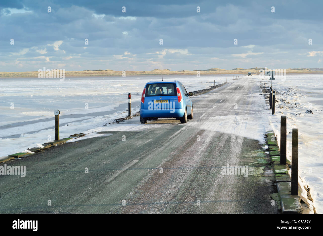 The tidal causeway road leading to Lindisfarne (Holy) Island with the mudflats covered by ice. Car vehicle driving. Stock Photo