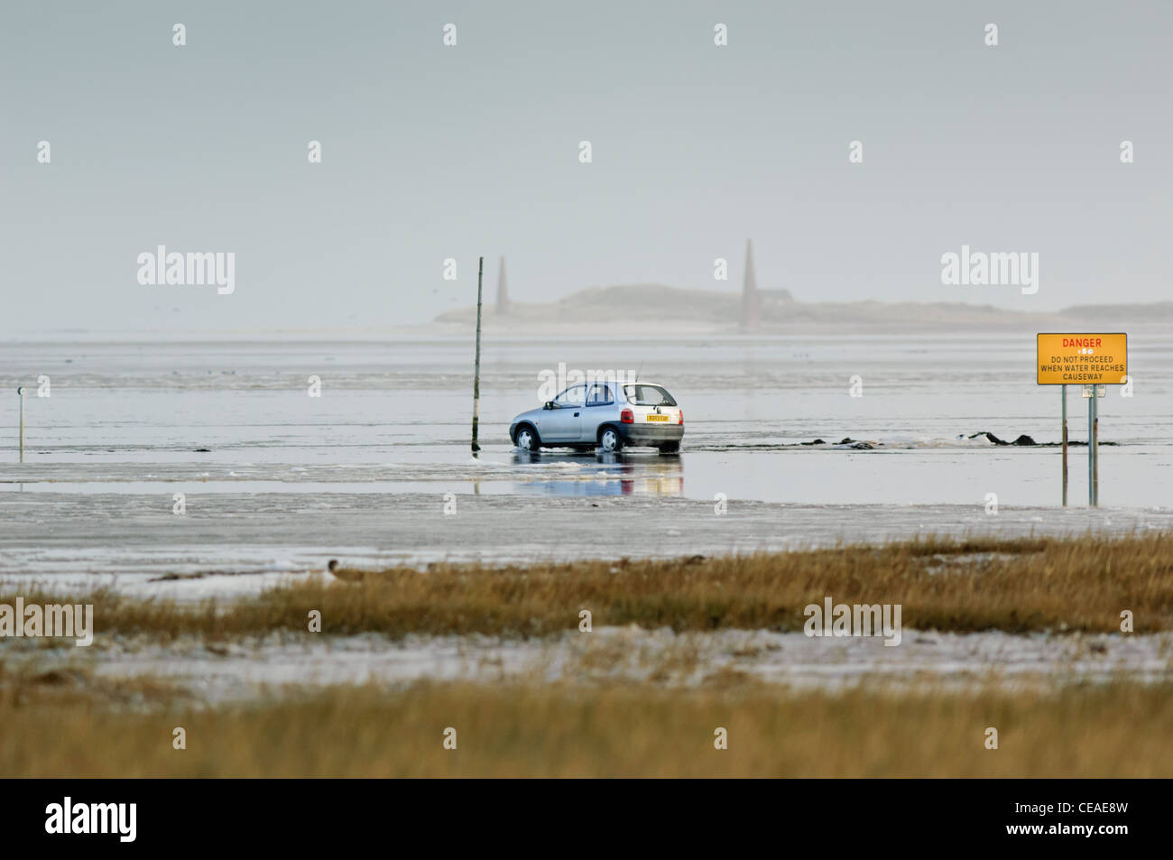 Car facing rising tide of icy water on the tidal causeway road leading to Lindisfarne (Holy) Island. Signage. Stock Photo