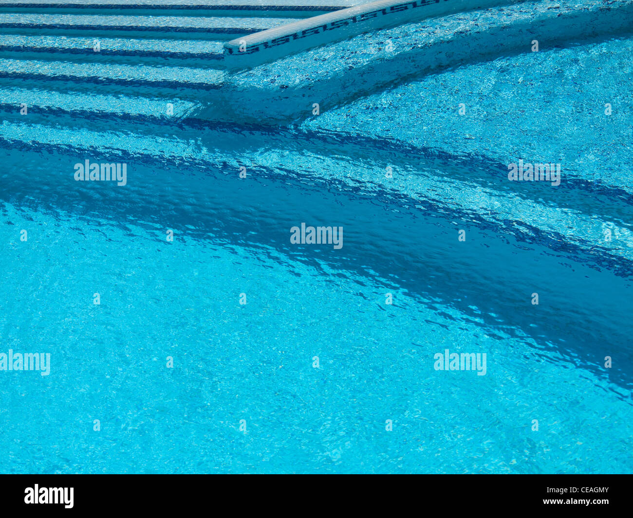 Turquoise swimming pool with steps, dark blue trim and rippling water. Stock Photo
