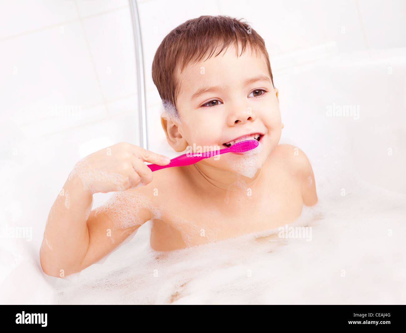 cute four year old boy taking a bath with foam and brushing teeth Stock