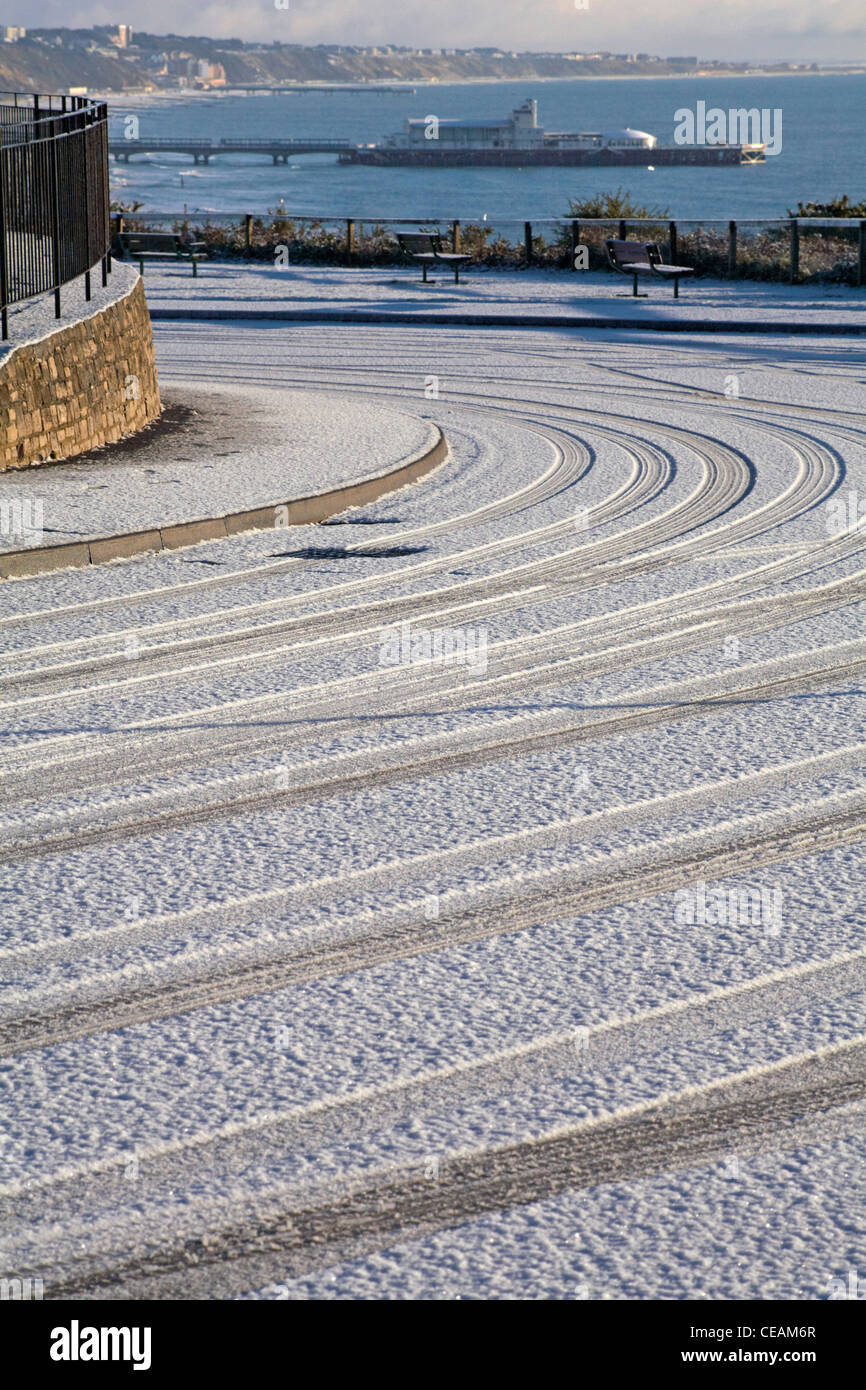 Tyre marks in the snow on a curved road where traffic has driven in West Cliff, Bournemouth with pier and sea in the distance Stock Photo
